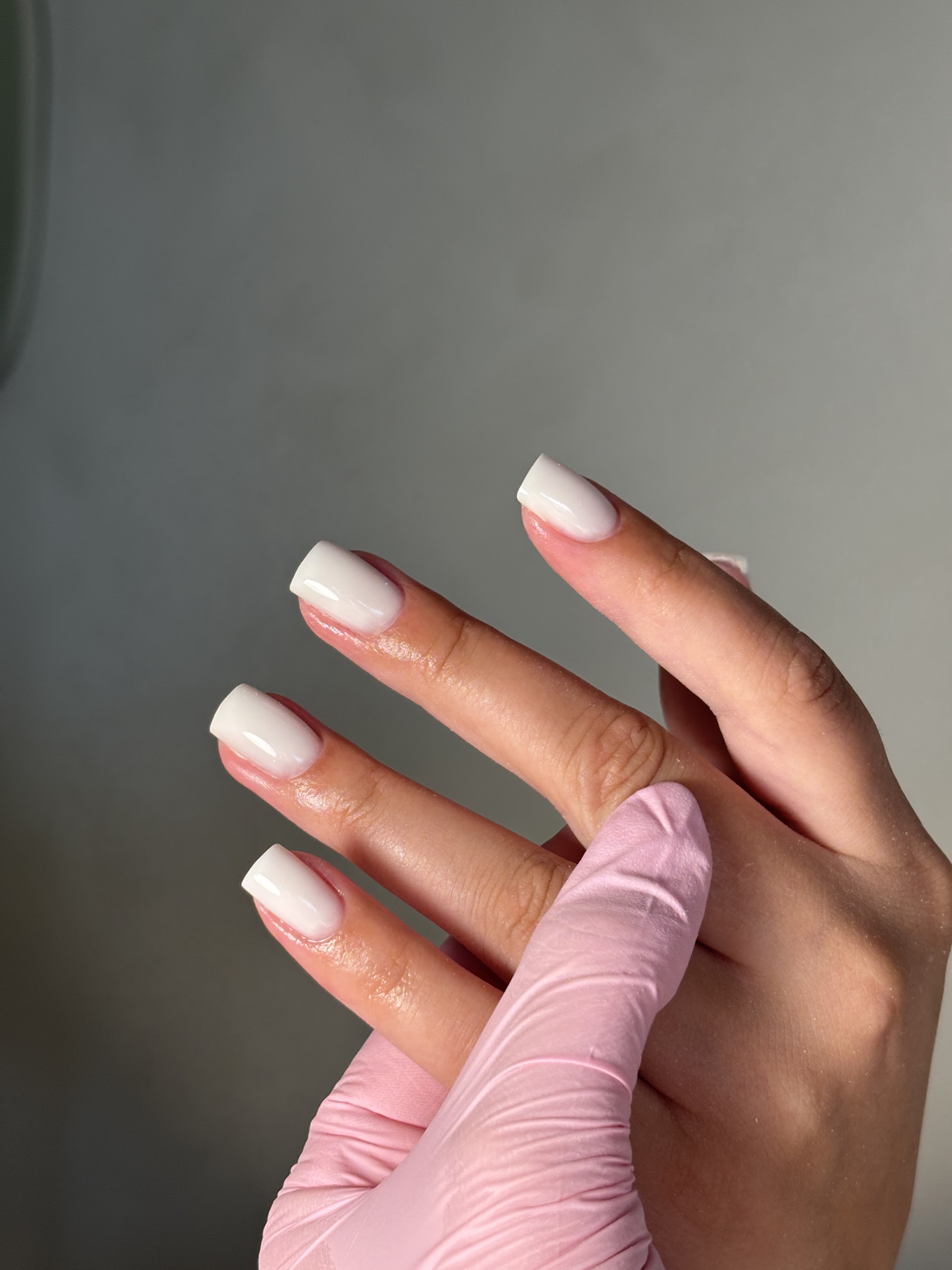 Melkwitte, vierkant gevijlde nagels naast een roze handschoen