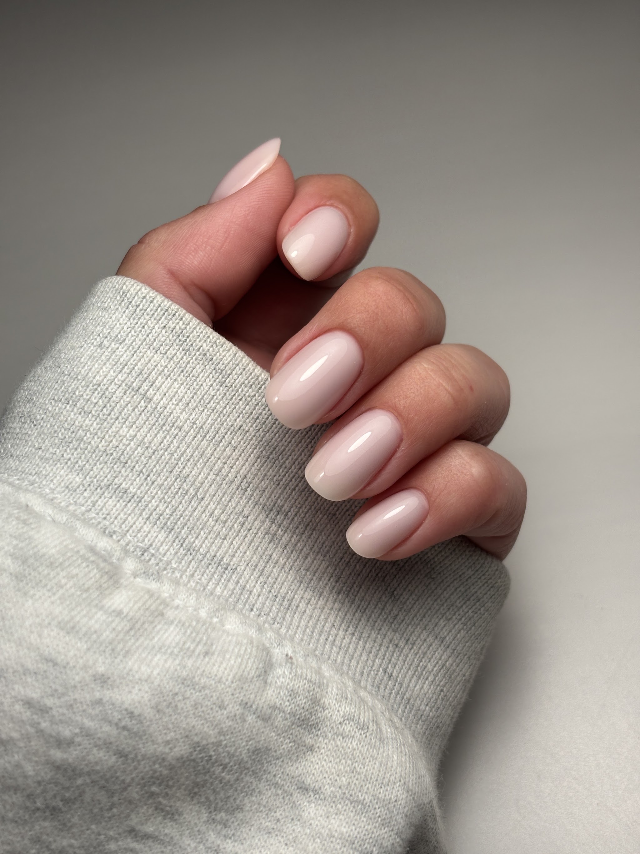Lichtroze, afgeronde nagels boven de mouw van een grijze trui